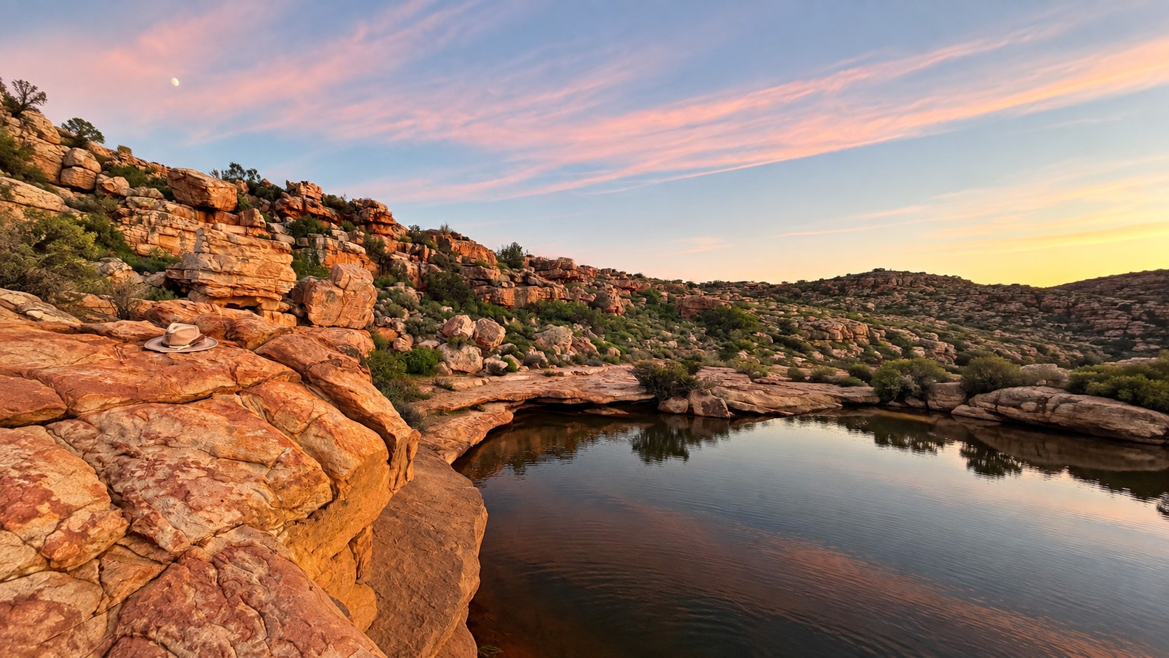 Sandstone rocks above a still pool at dusk, a fedora resting on a boulder beneath a streaked sky