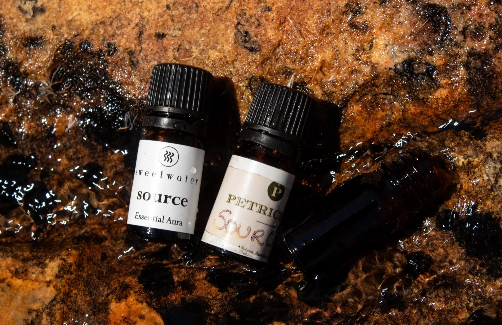 Three amber bottles resting on a wet rock face, water running over the stone