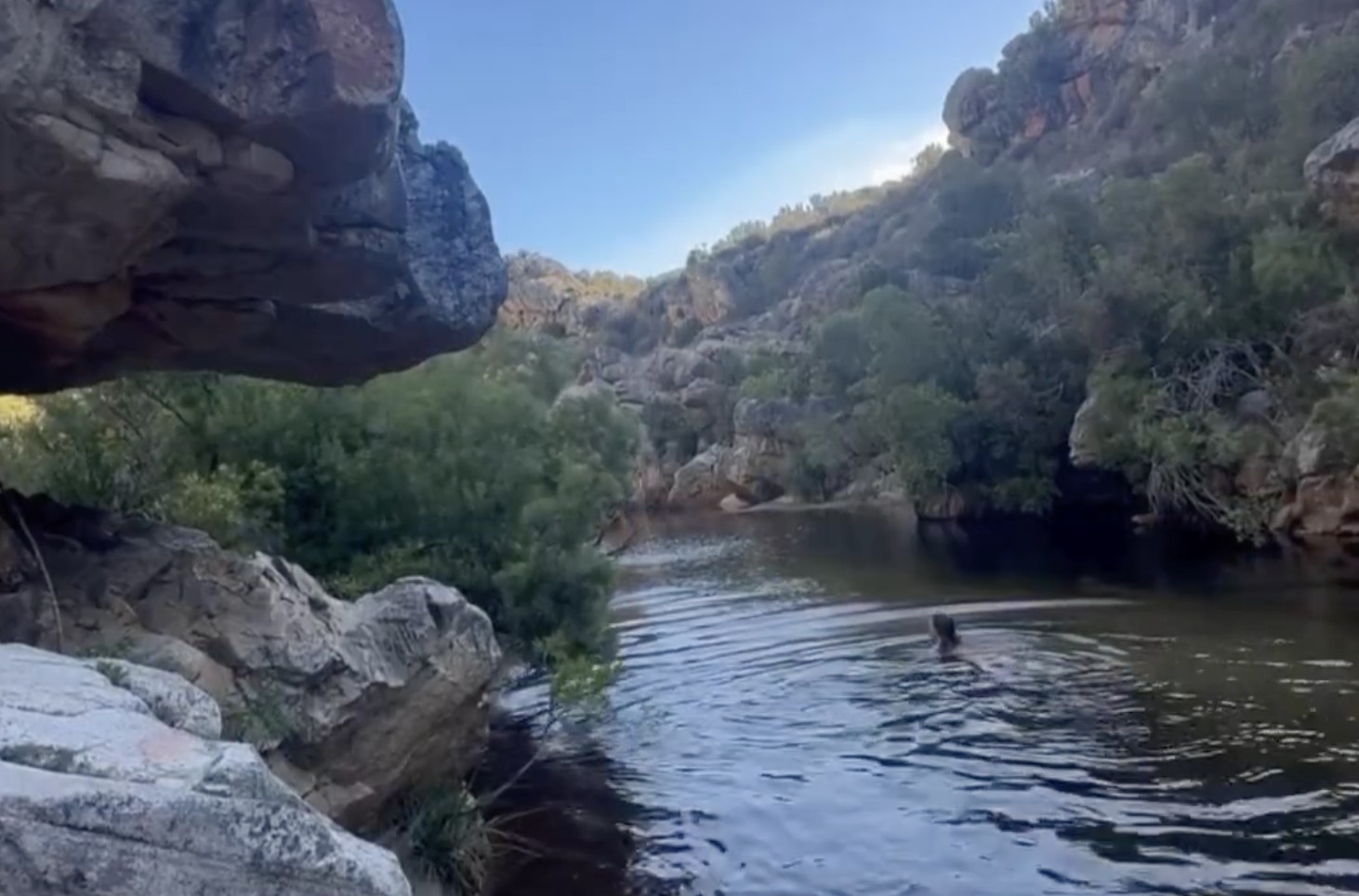 A swimmer moving through a dark mountain rock pool held between canyon walls